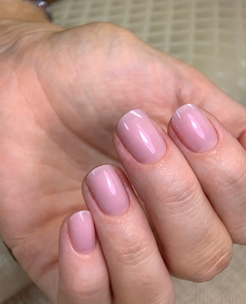 Aplicação técnica de esmaltação em gel com unhas rosadas brilhantes e acabamento impecável.